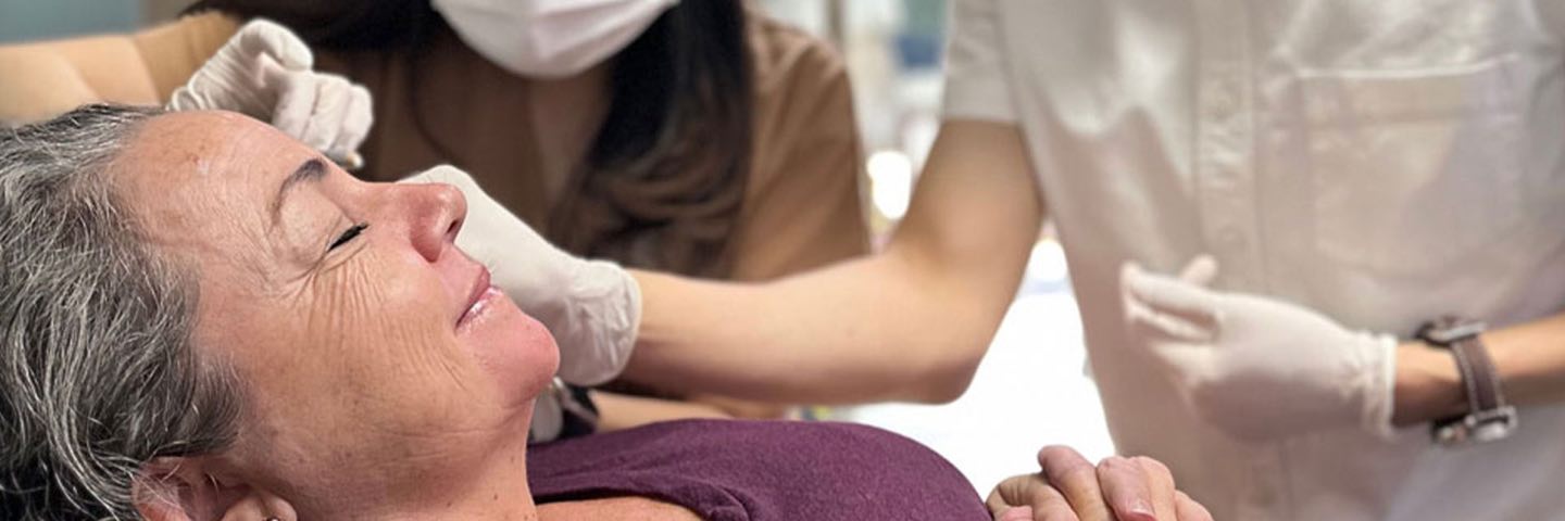 A Cocoon doctor and nurse, both in masks and gloves, preparing a smiling guest’s face for treatment