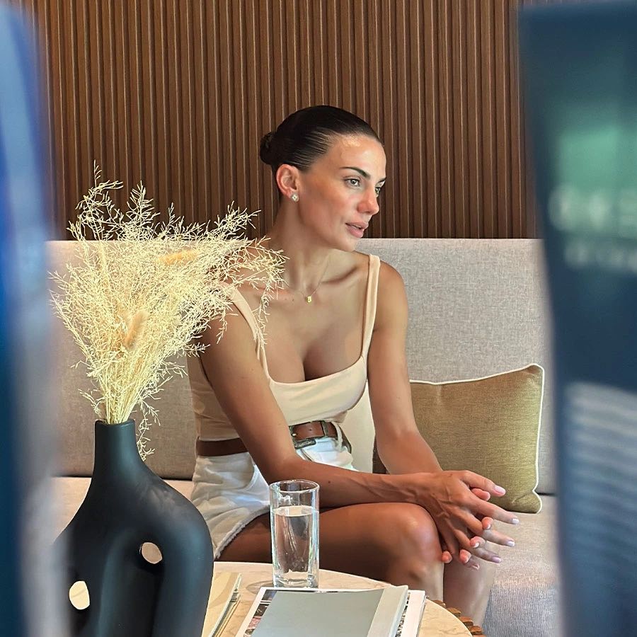 A guest seated on a cream sofa in the Cocoon lounge, beside a vase of dried flowers and a glass of water