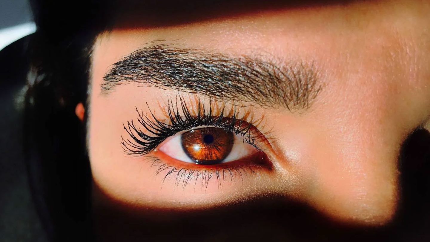 A close-up of a woman’s eye with long lashes and a defined brow