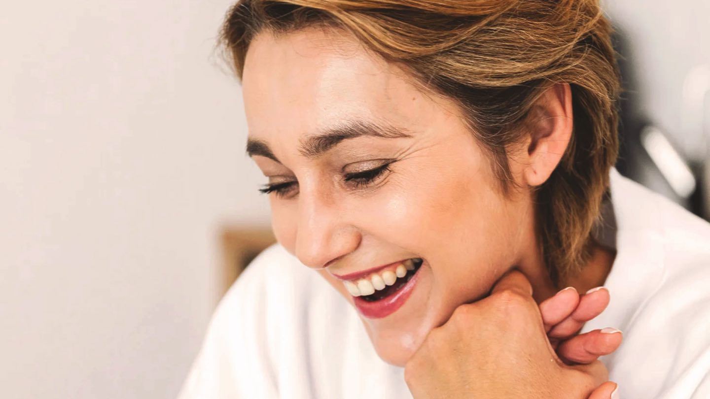 A smiling woman resting her chin on her hand, her skin even-toned