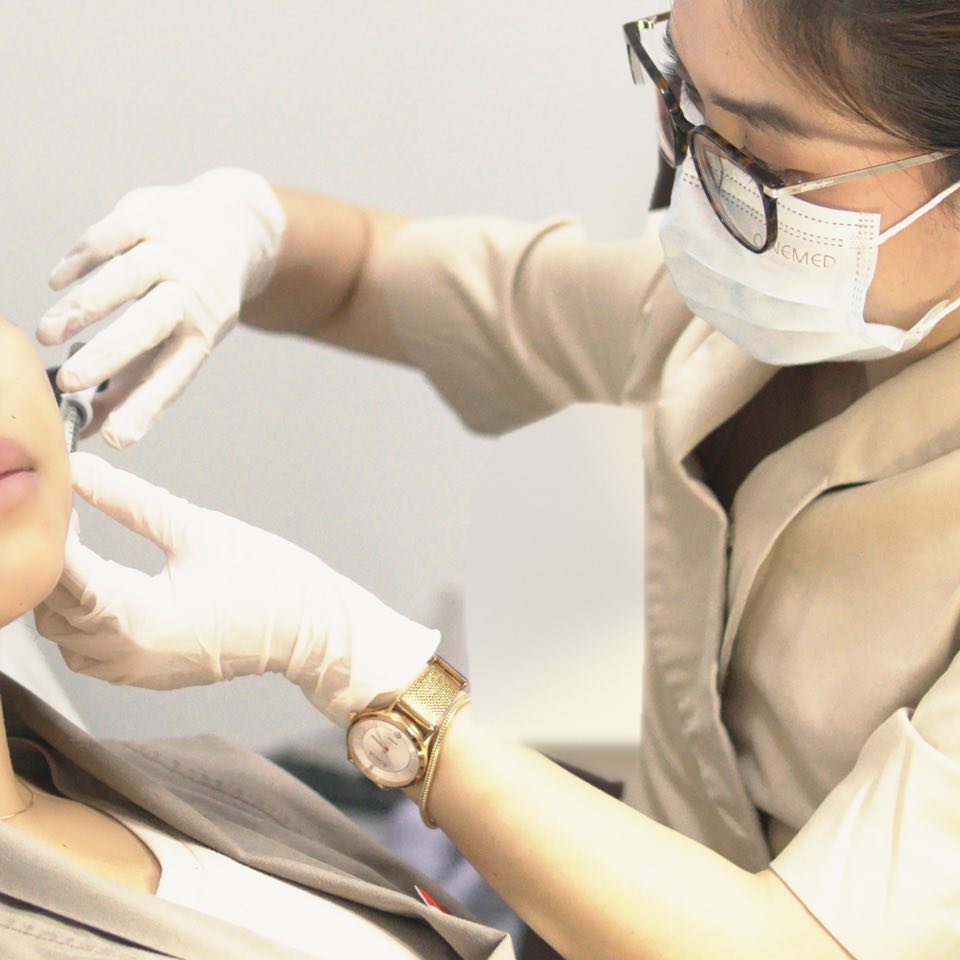 The doctor’s gloved hands steadying the syringe at the guest’s cheek