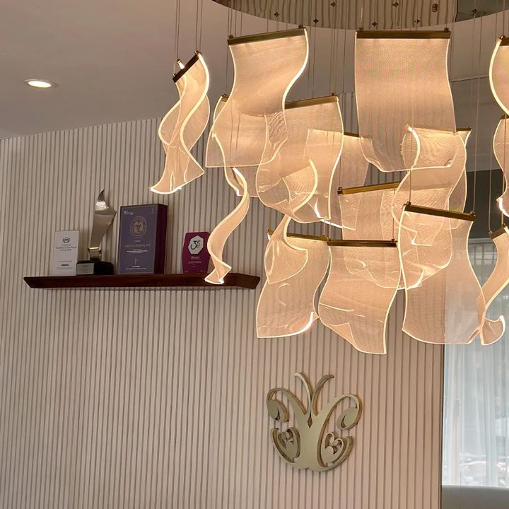 Cocoon reception: a glowing ribbon chandelier above the gold Cocoon butterfly logo and a shelf of the clinic's awards