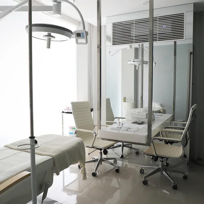 A Cocoon Canggu consultation room: a desk and two chairs beside a treatment bed under a surgical light