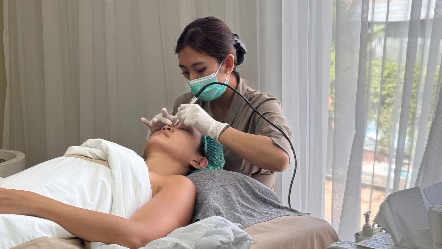 A Cocoon therapist in a mask and gloves treating a guest’s skin in a bright treatment room at the Canggu clinic
