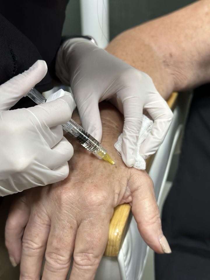 Gloved hands giving a skin booster injection into the back of a client’s hand at Cocoon