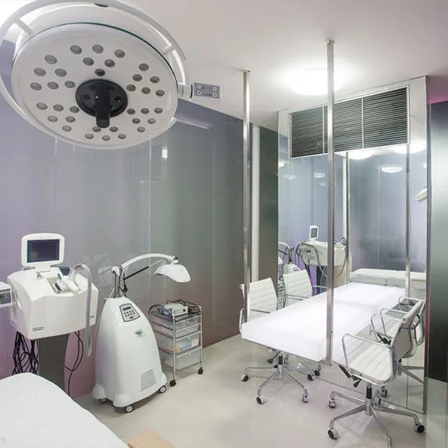 A treatment room at Cocoon Legian: a bed under a surgical light, glass walls