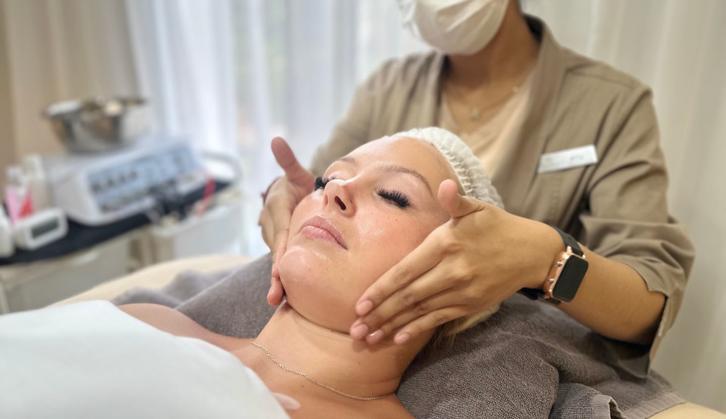 A masked Cocoon therapist massaging a guest’s jaw and cheeks during a facial