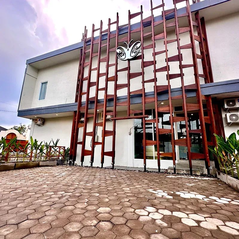 The Cocoon Canggu building: a timber lattice facade with the gold butterfly logo above a paved forecourt