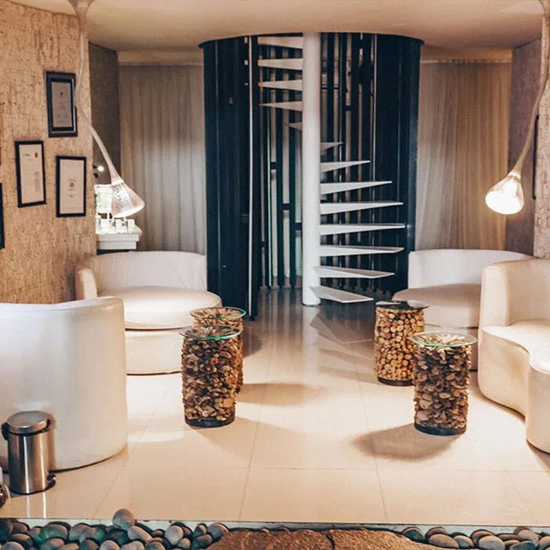A lounge with cream tub chairs and timber side tables beside a white spiral staircase