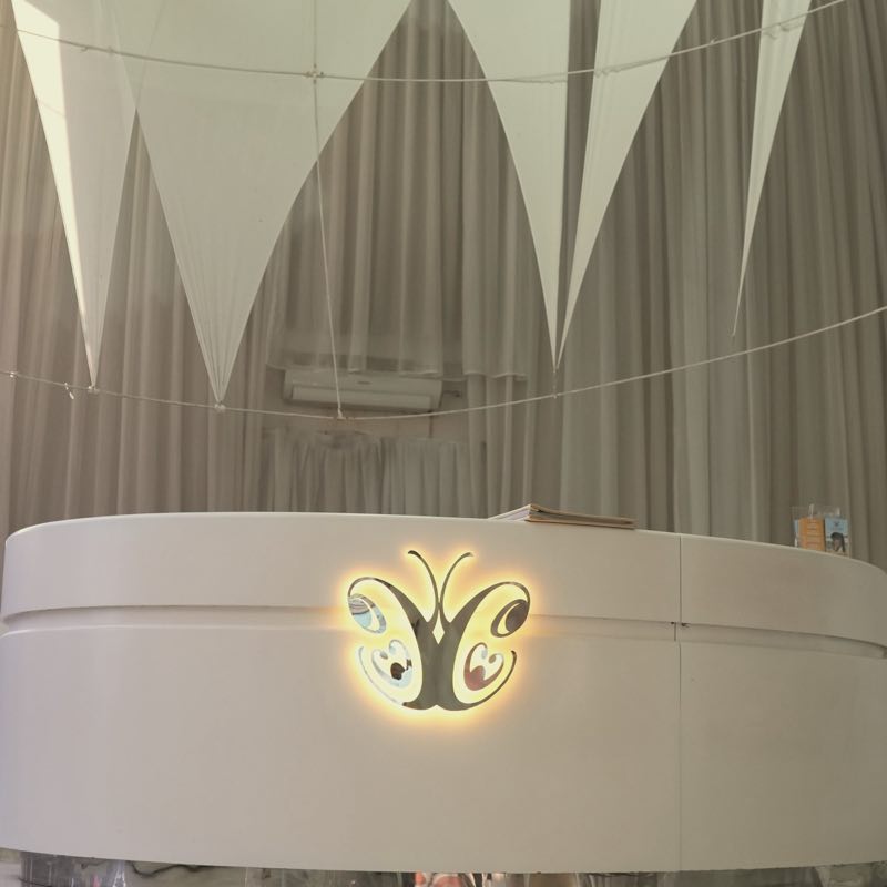 The Legian reception under its high ceiling: white fabric sails above the curved desk, its butterfly logo lit gold