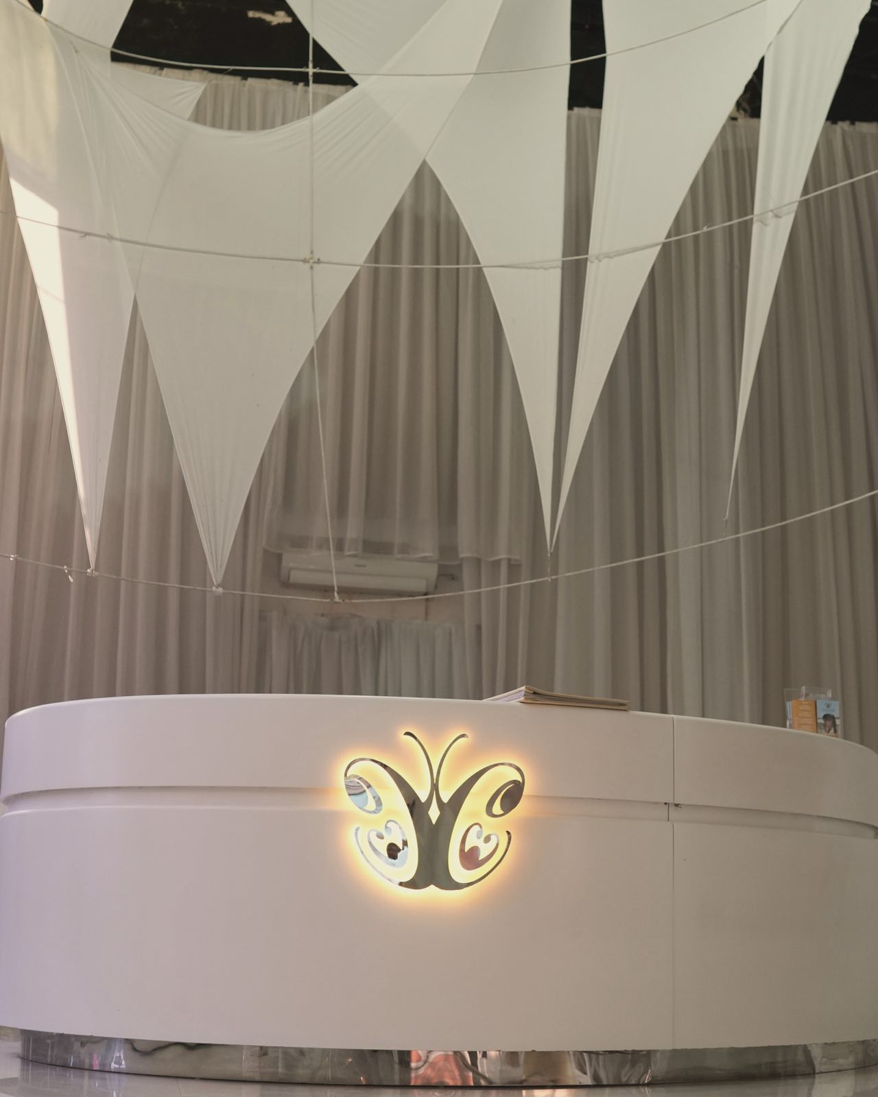 The Legian reception under its high ceiling: white fabric sails above the curved desk, its butterfly logo lit gold