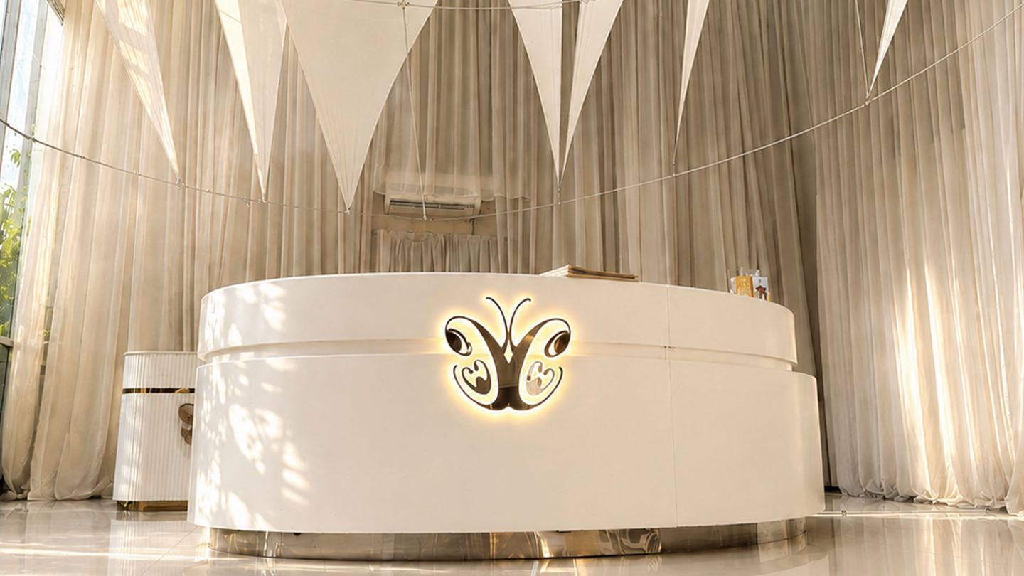 The Cocoon Legian reception: a curved white desk with the gold butterfly logo, beneath a pale fabric canopy