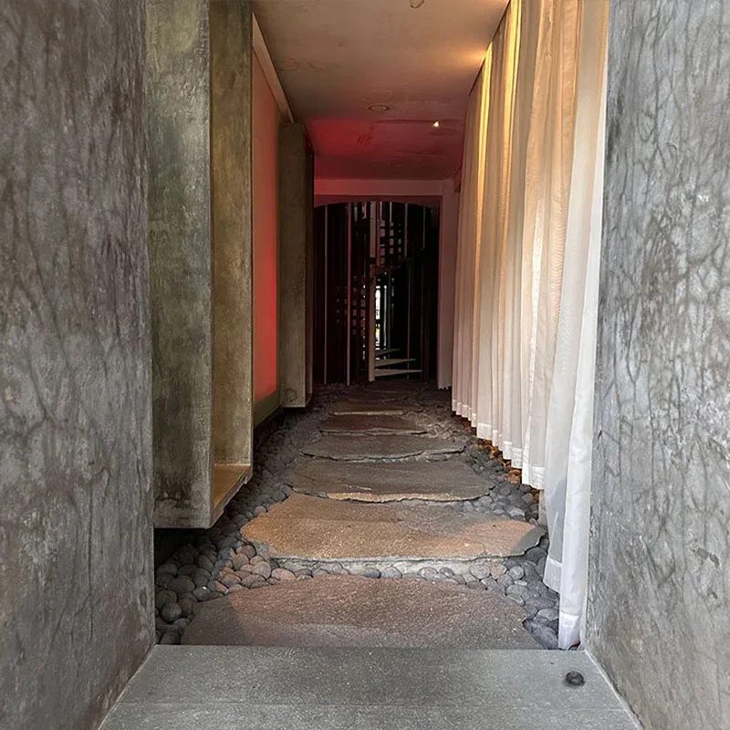A stone path between rough concrete walls and soft curtains, lit warm at the far end