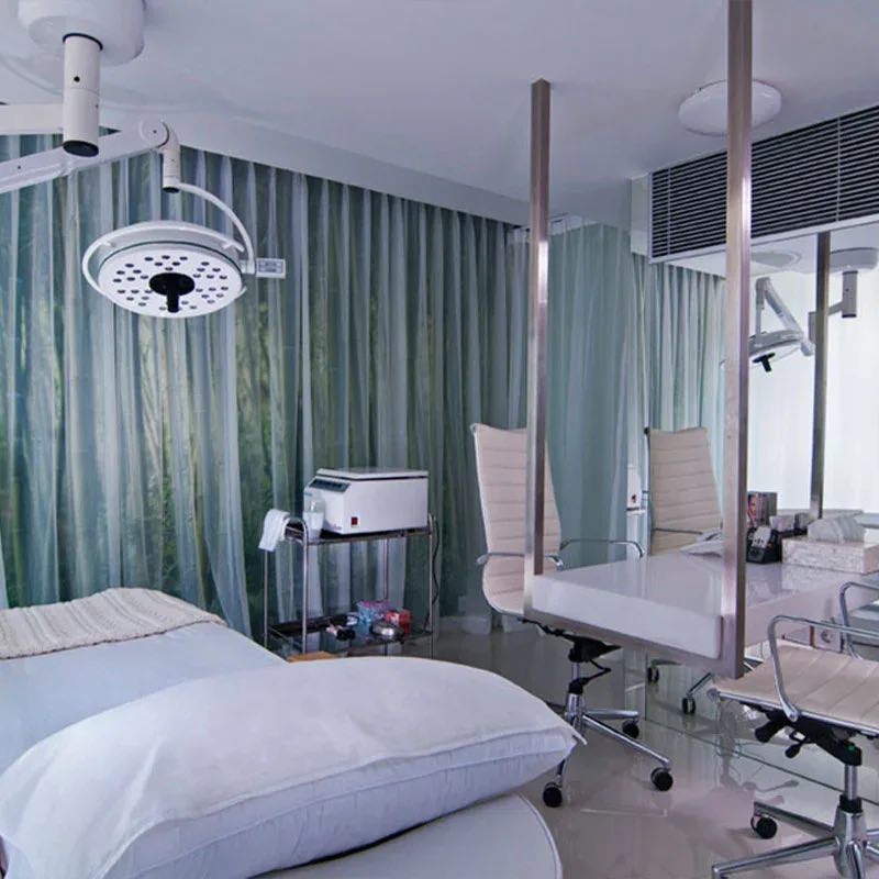 A treatment room at Cocoon Ubud: a white bed, a surgical light and a desk behind glass