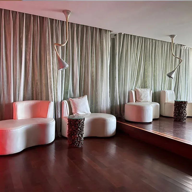 Pale pink tub chairs and pendant lamps in the Ubud lounge, framed by long linen curtains