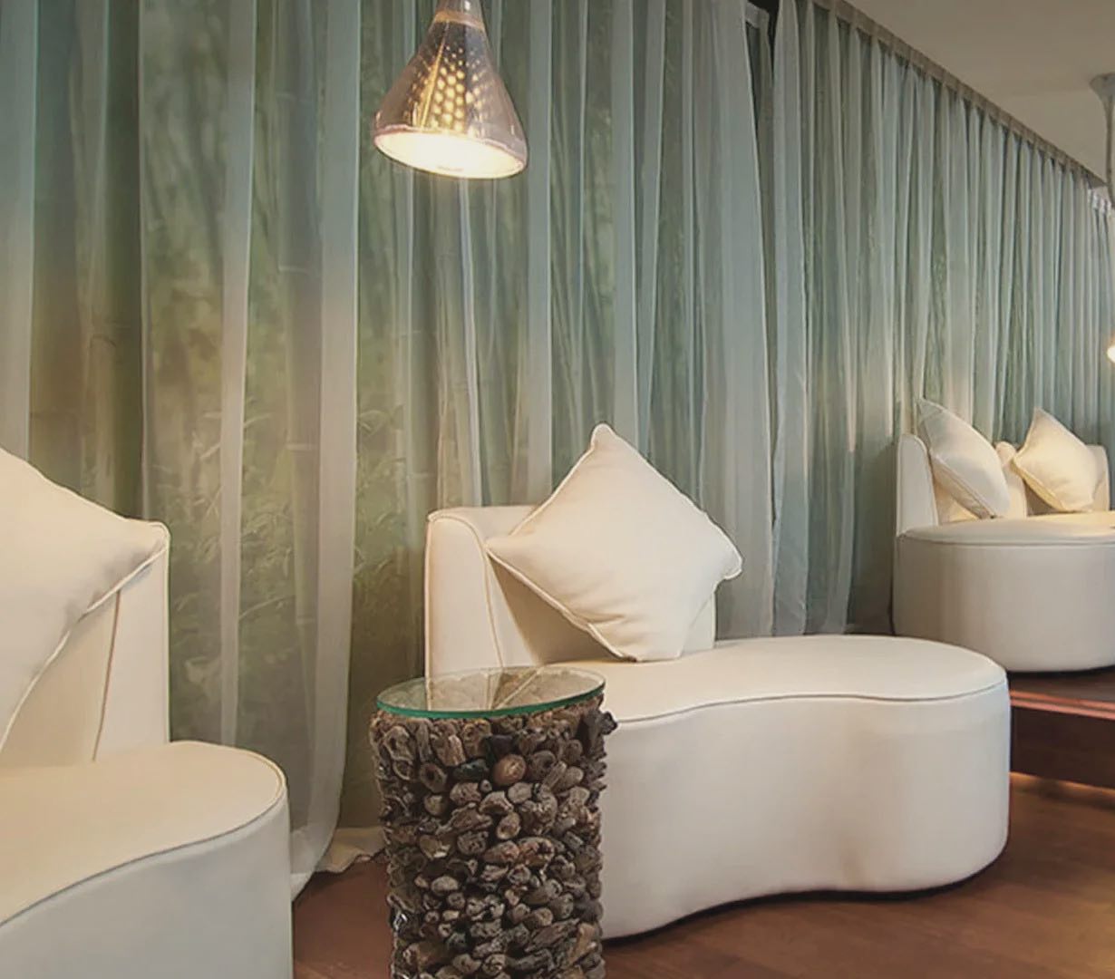 The Cocoon Ubud relaxation lounge: cream curved sofas, pendant lamps and a glass wall onto a green rice field