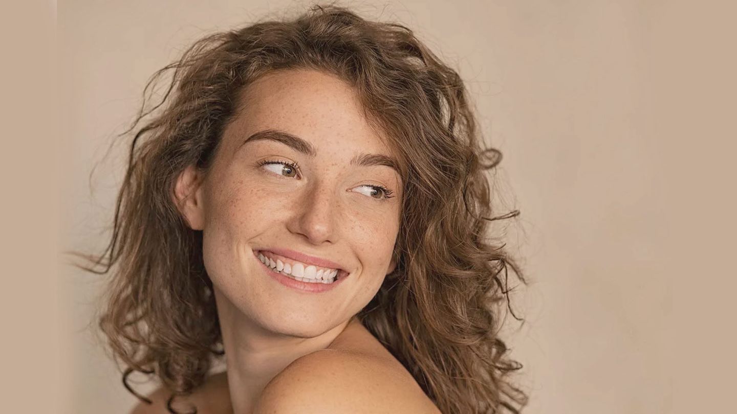 A smiling woman with curly hair looking over her shoulder