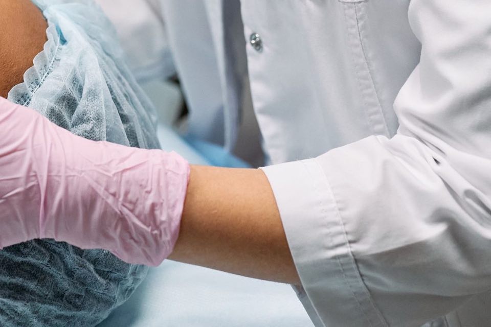 A clinician’s pink-gloved hand gently supports a patient’s head as she rests on the treatment bed.