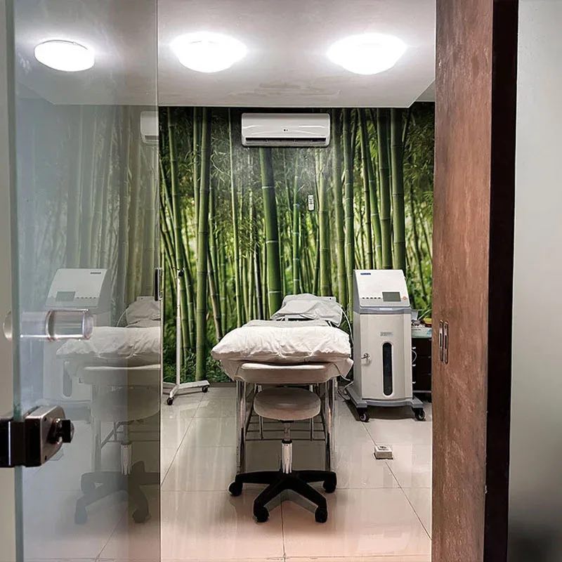 A Cocoon Ubud treatment room with a bamboo-forest wall, a treatment bed and a medical device