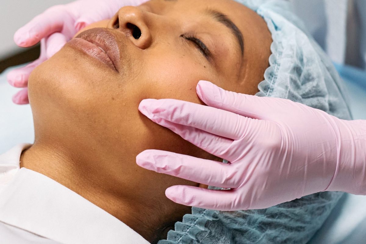 Close-up of a relaxed woman with her eyes closed as a clinician’s pink-gloved hand rests along her cheek.