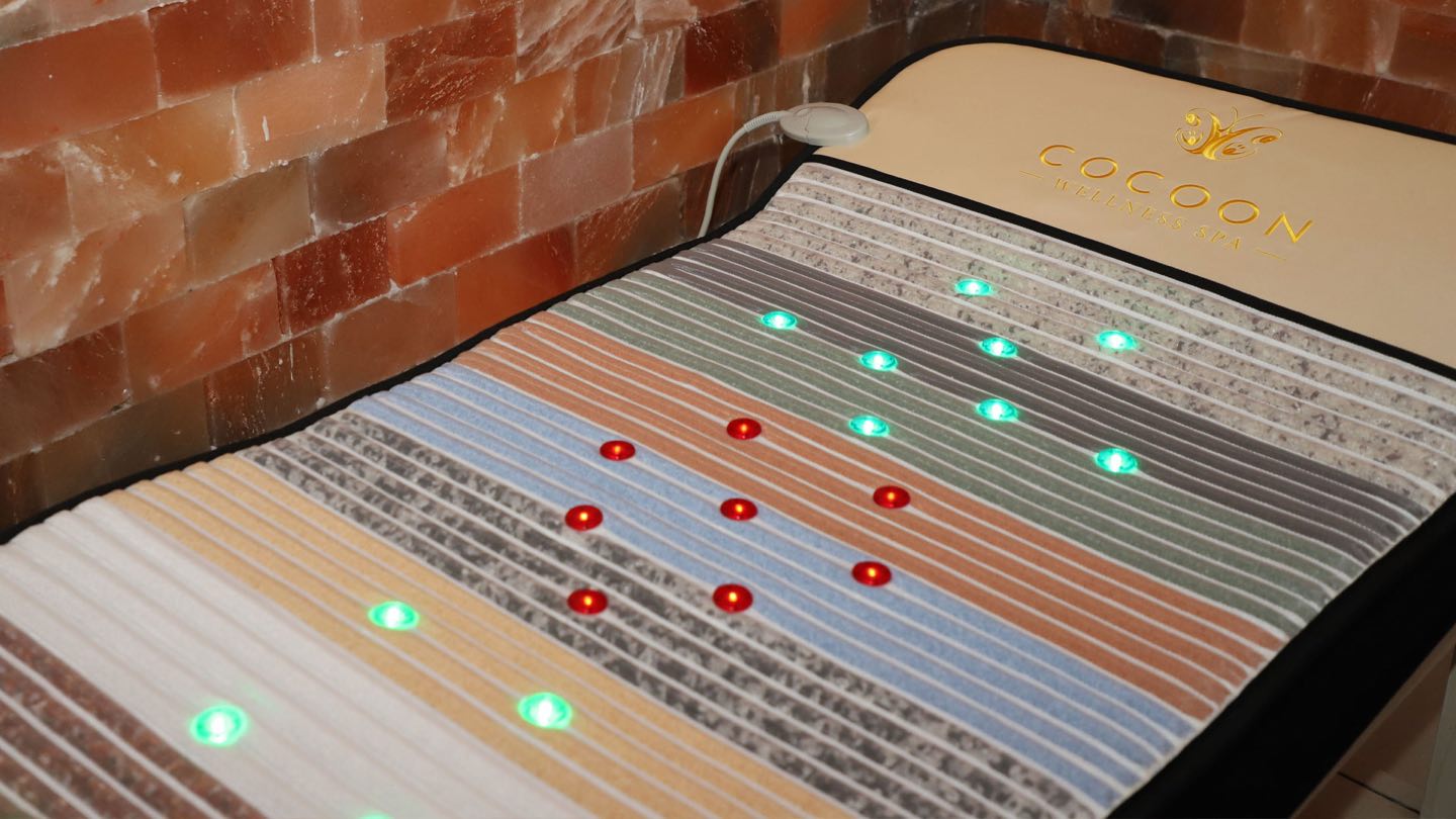 The Cocoon Crystal Tourmaline PEMF Biomat laid out in front of a Himalayan salt-brick wall