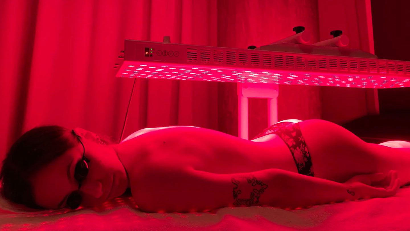 A guest lying face-down under a red light panel in a red-lit room, wearing eye protection